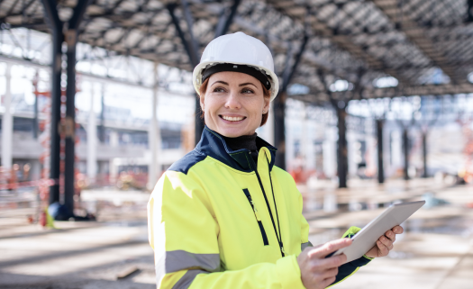 Contractor using construction management software on a tablet, standing on a construction site